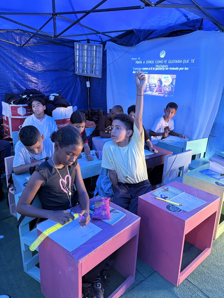 Niños en pupitres dentro del aula en la carpa
